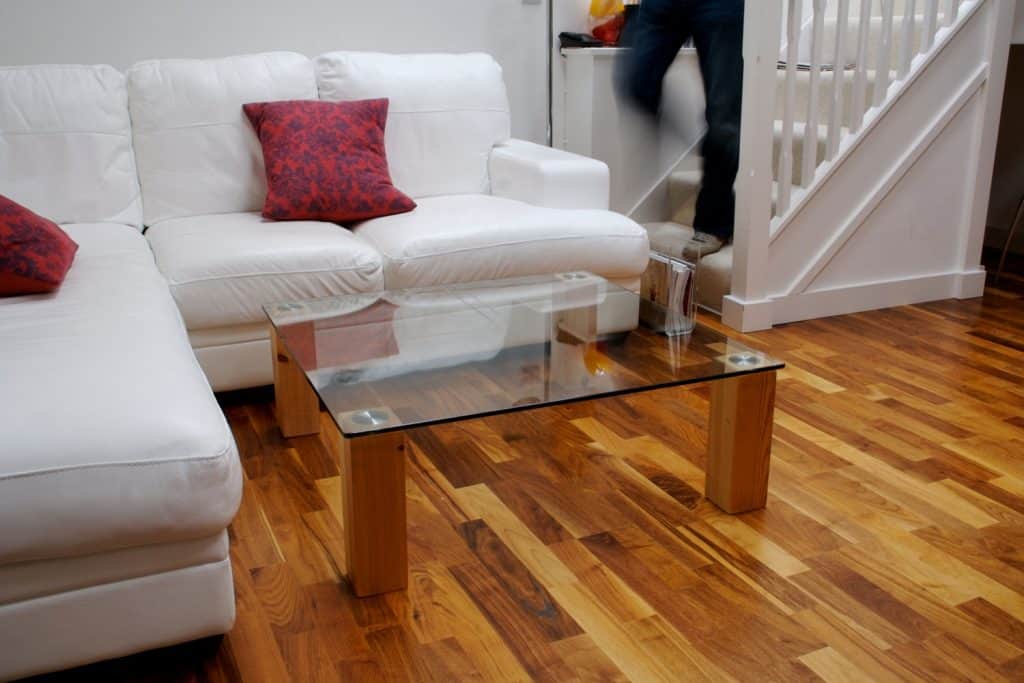 A gorgeous light themed living room with hardwood flooring and a small glass with wooden leg coffee table