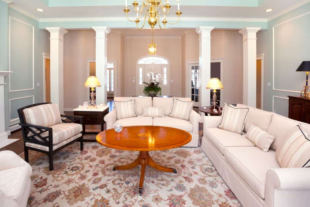 An old Victorian themed living room with white sofas, a carpet with floral design, and a tall wooden center coffee table