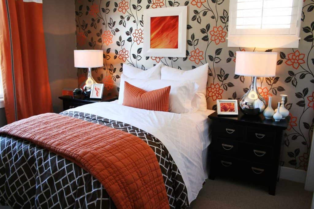 A gorgeous floral accent wall with white beddings and an orange curtain