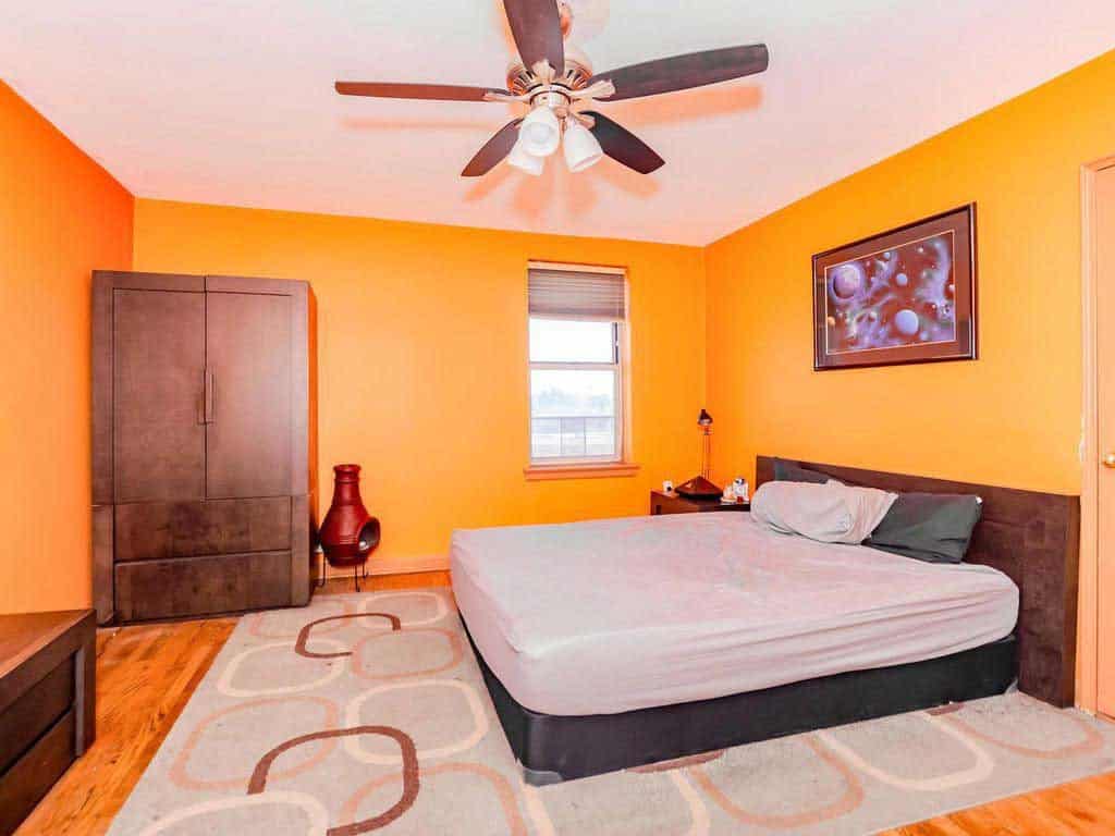 A huge orange wall bedroom with hardwood flooring, huge wooden China cabinet, and a white bed