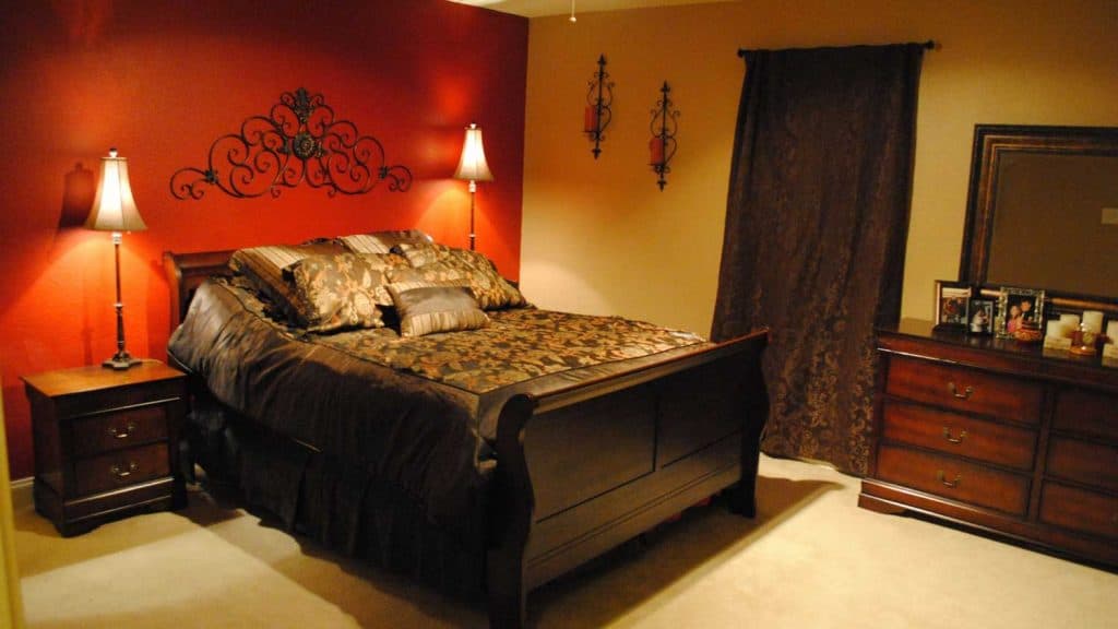 A dark inspired bedroom with a huge dark bed with a red accent wall