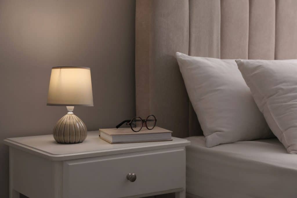 A light gray bedside table and matching white bed