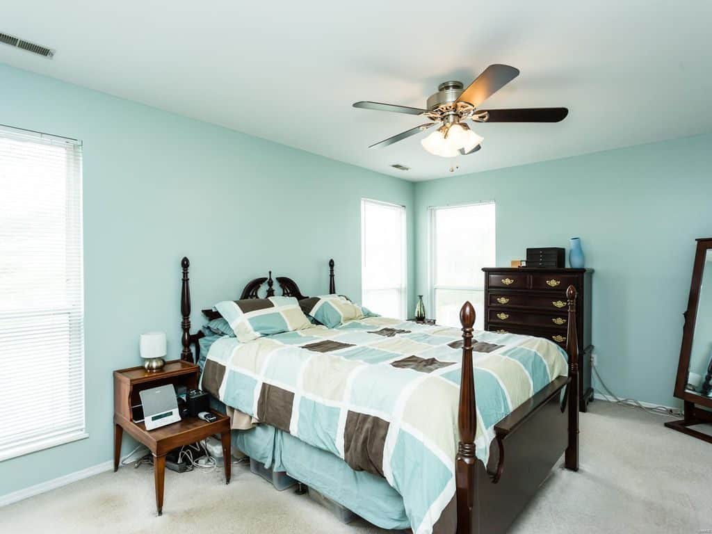 Modern teal painted bedroom walls, dark wooden oak bed with teal beddings, and a ceiling fan