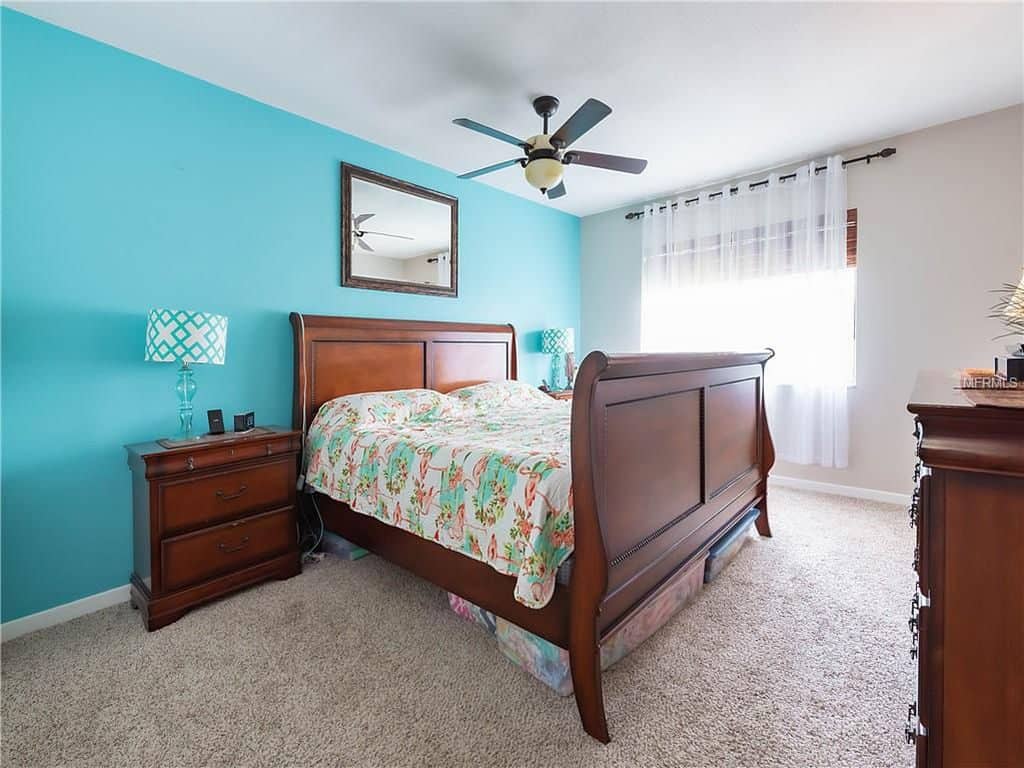 Interior of a spacious bedroom with a teal painted wall, carpeted flooring, and a huge wooden oak bed