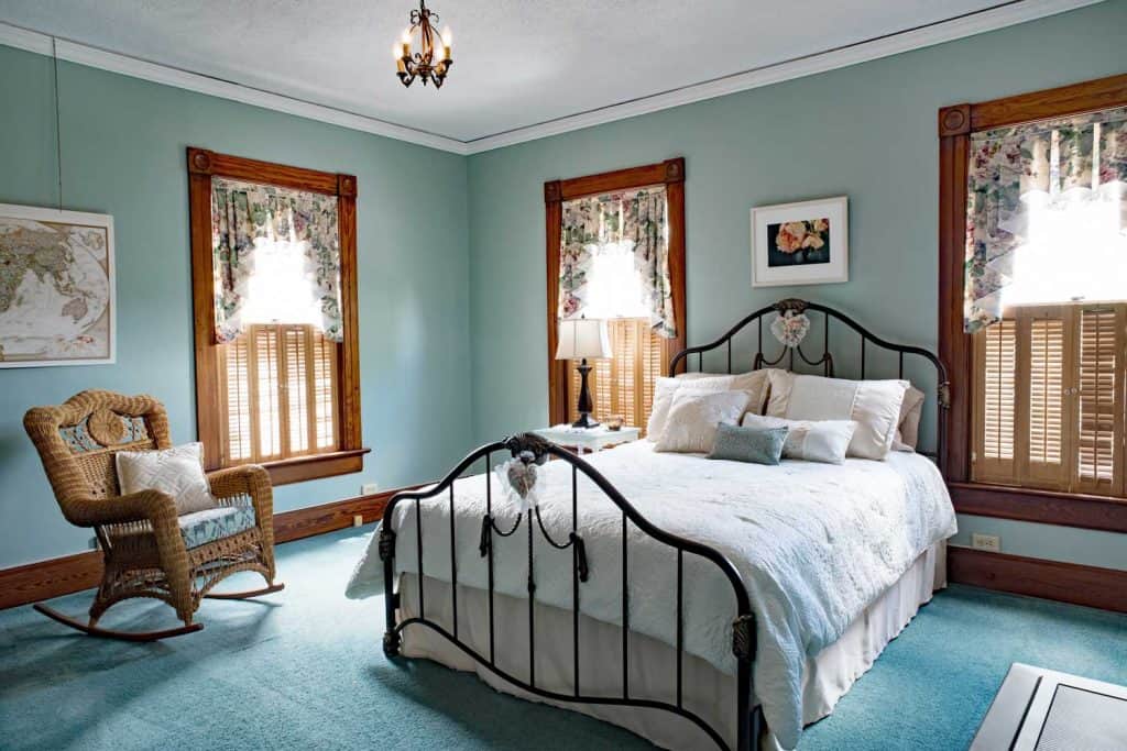 Interior of a rustic themed bedroom with teal colors, teal carpeted flooring, and a metal framed bed
