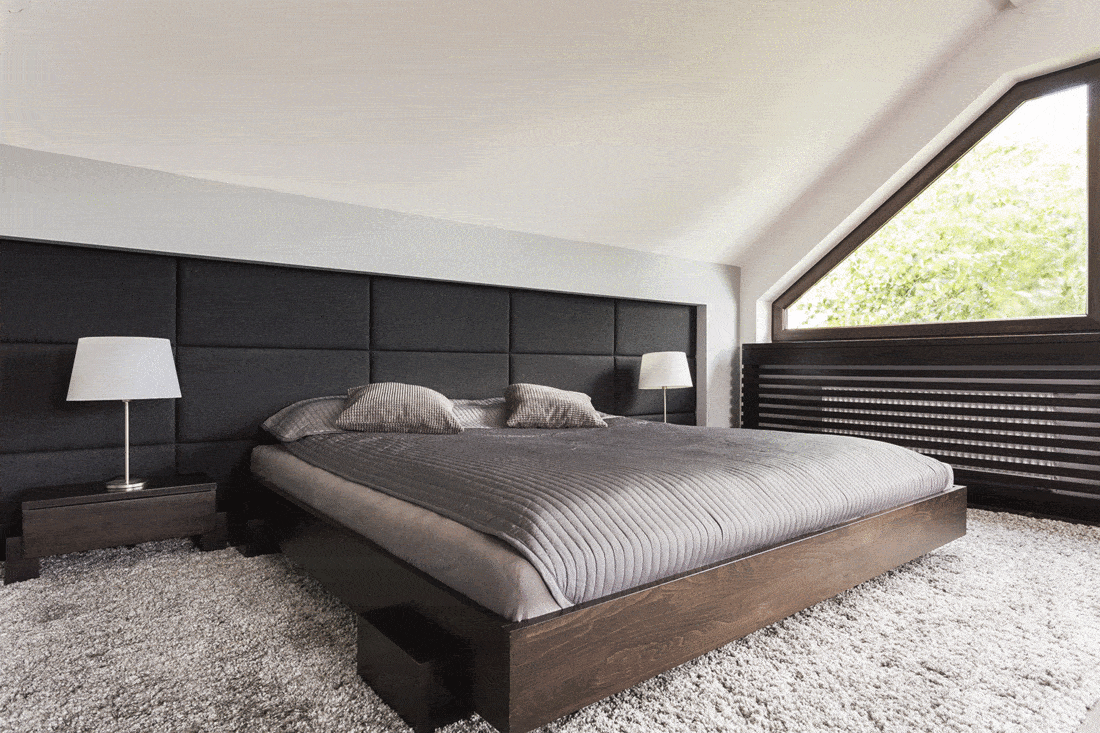 Elegant large bed in a dark frame in an attic bedroom