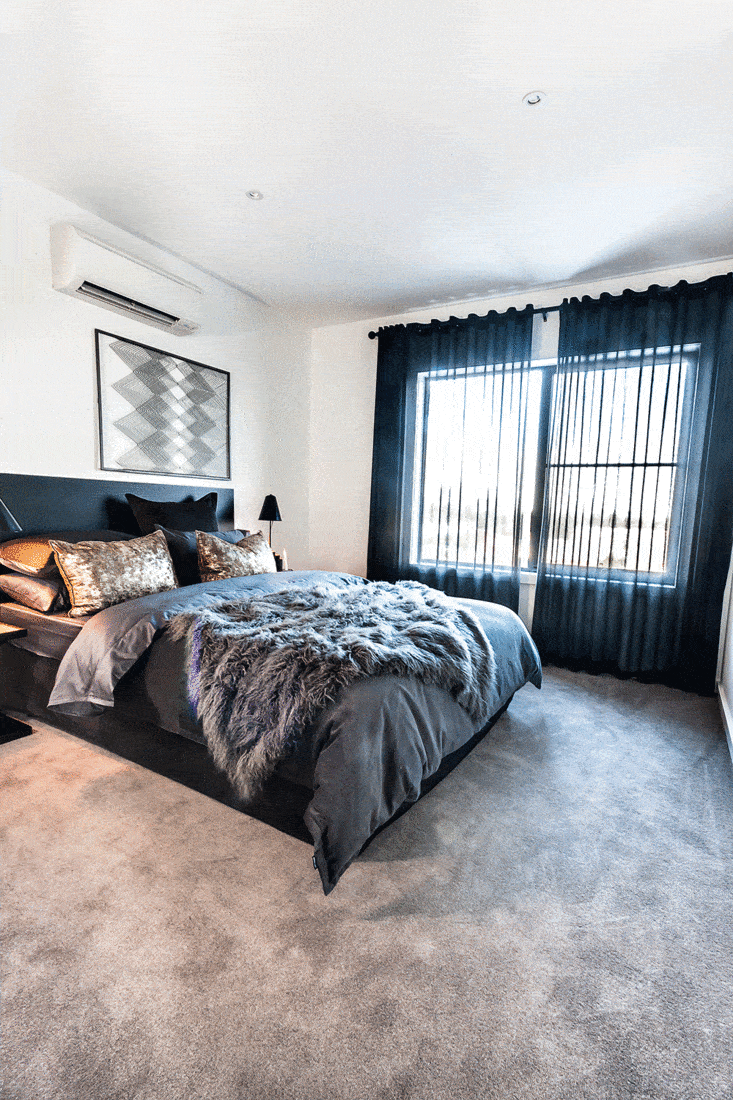 Modern bedroom with a carpet floor space illuminated using sunlight and decorated using dark bedding items