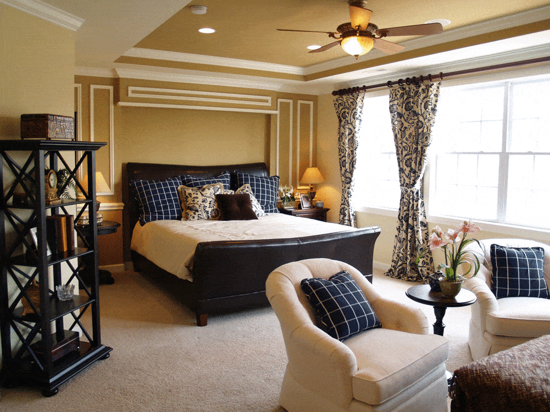 Nicely decorated master bedroom in a newly built luxury home. There is a black leather sleigh bed, dark furniture, light streaming through the windows