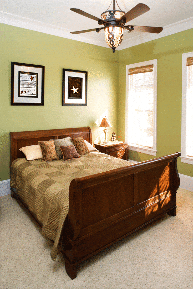 Sleigh bed in a green bedroom with a ceiling fan and wall art