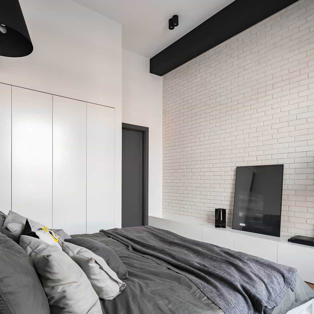 Bedroom with white brick wall and bed with grey sheet, pillows and blanket