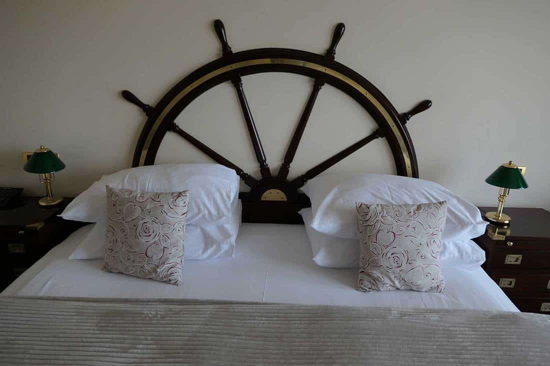 A wooden ship wheel on a small bed with white pillows