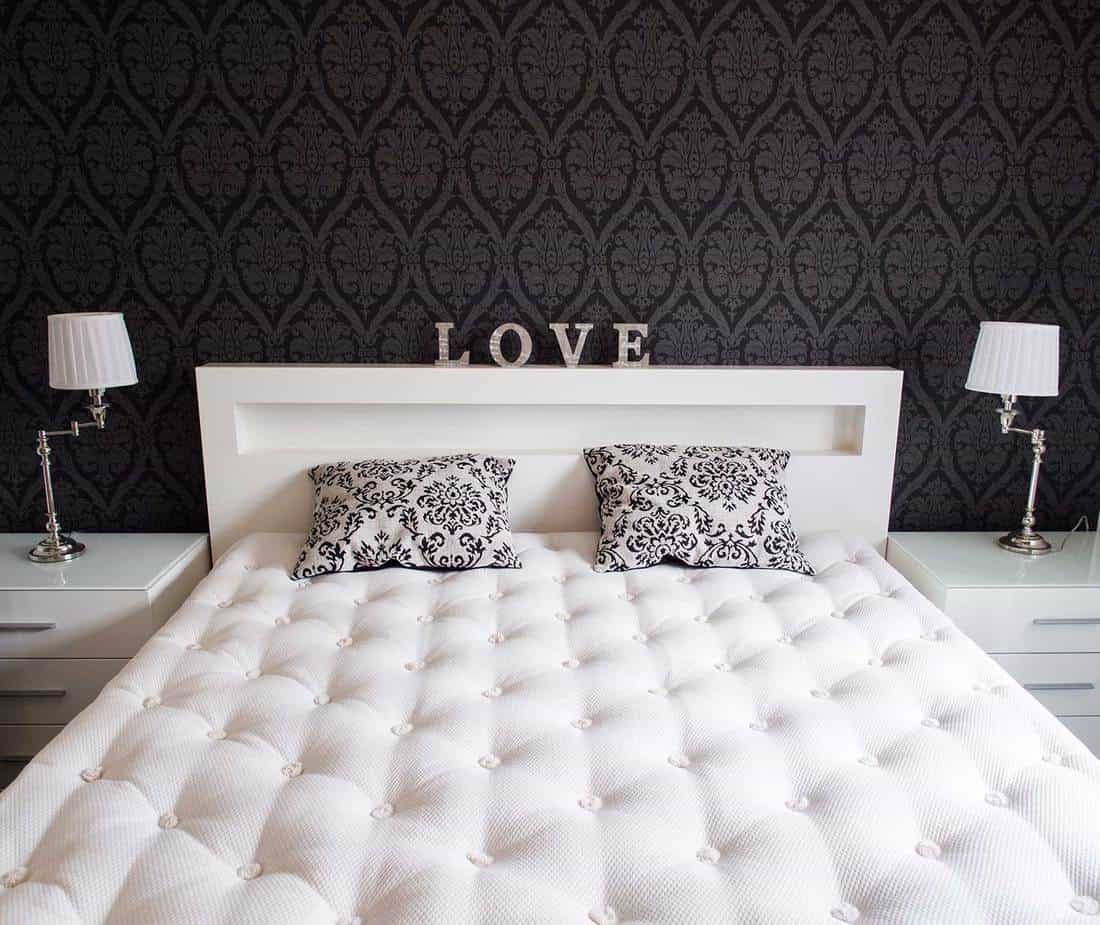 Two black and white patterned pillows on white mattress bed between white lamps