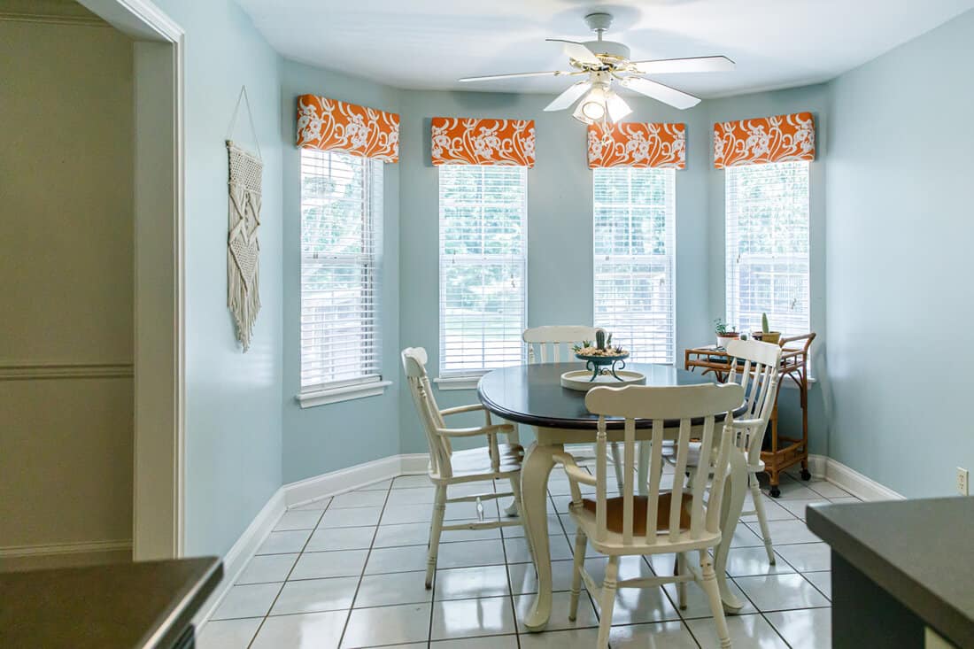 A bay windowed kitchen with walls painted in a light blue and matched with flower valance curtains