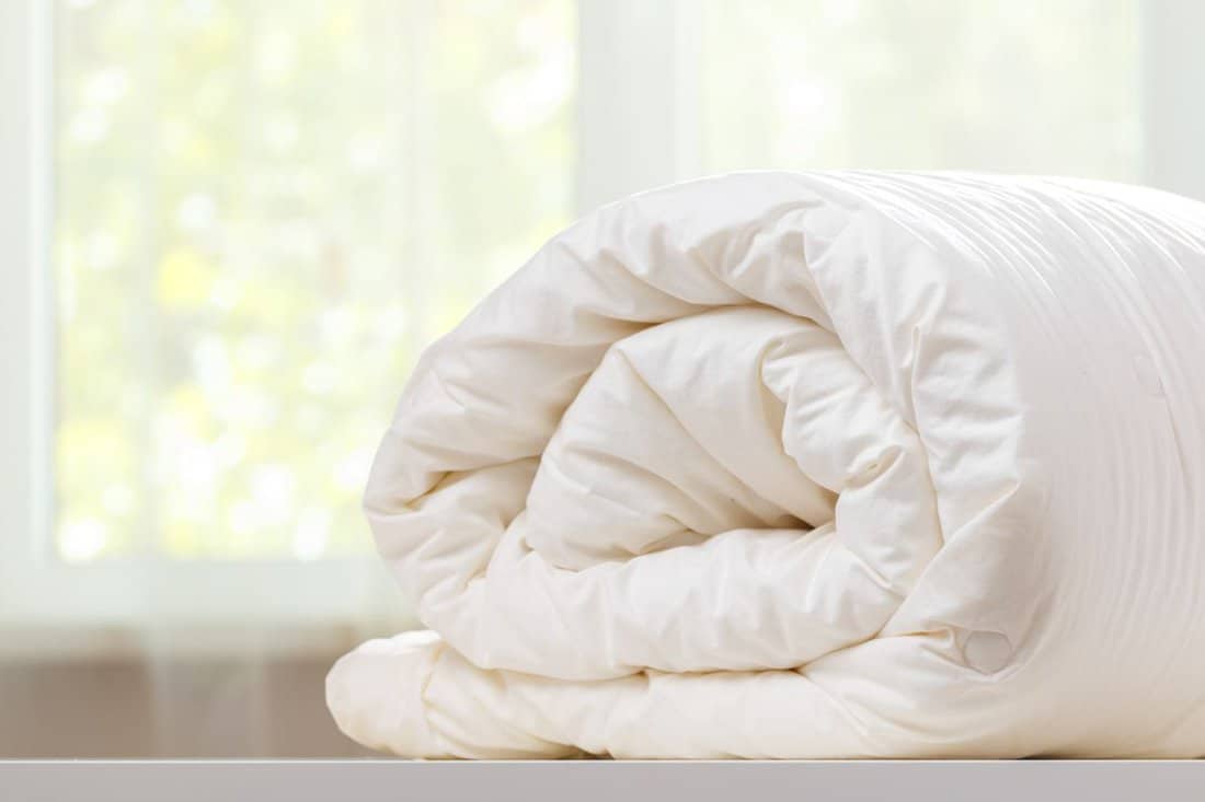 A folded rolls duvet is lying on the dresser against the background of a blurred window. 