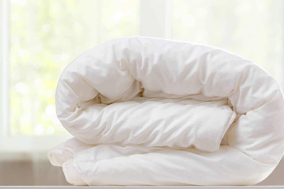 A folded white duvet lies on a table on a blurred background