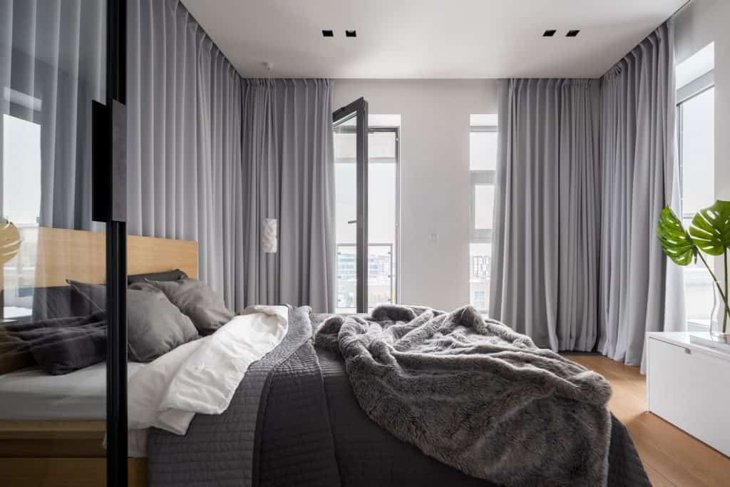A large gray themed bedroom with gray beddings, gray floor length curtains, and an indoor plant on the bookshelf
