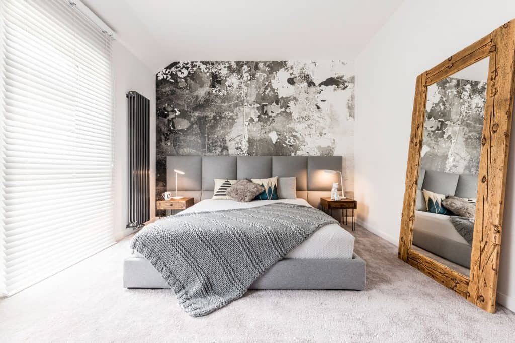 A narrow farmhouse themed bedroom with gray beddings, gray pillows, and an abstract wall design