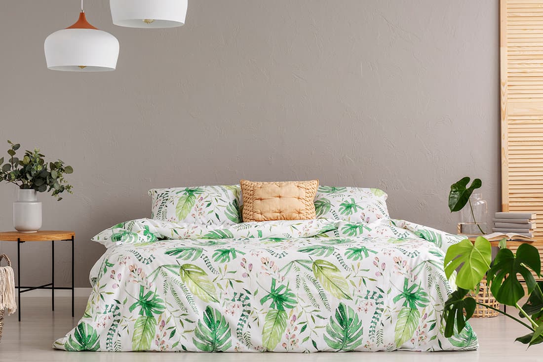 Green flower in vase on nightstand next to king size bed with floral bedding and peach colored pillow,