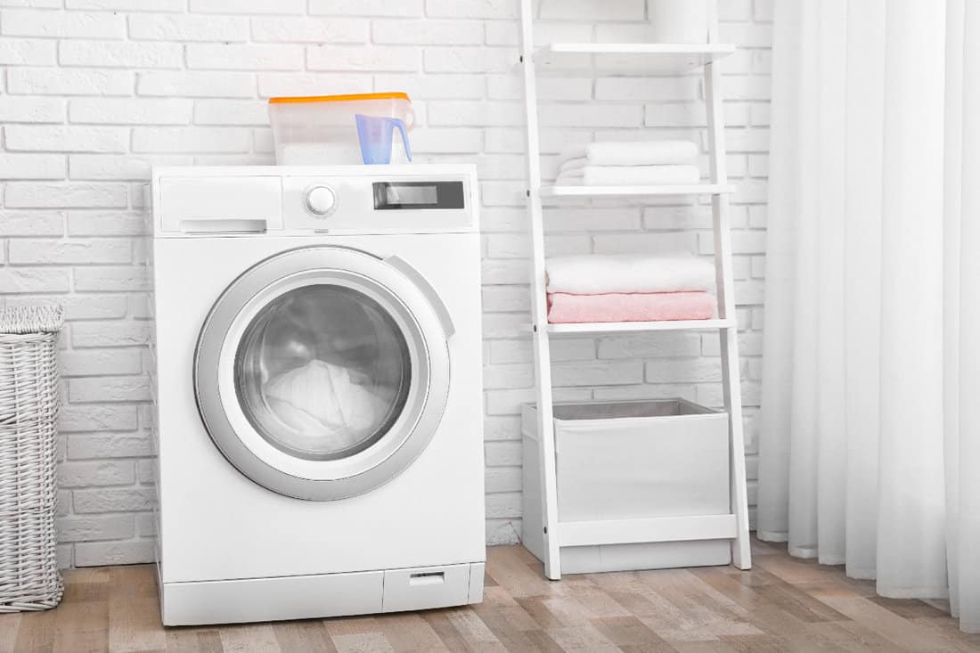 Modern washing machine near brick wall in laundry room