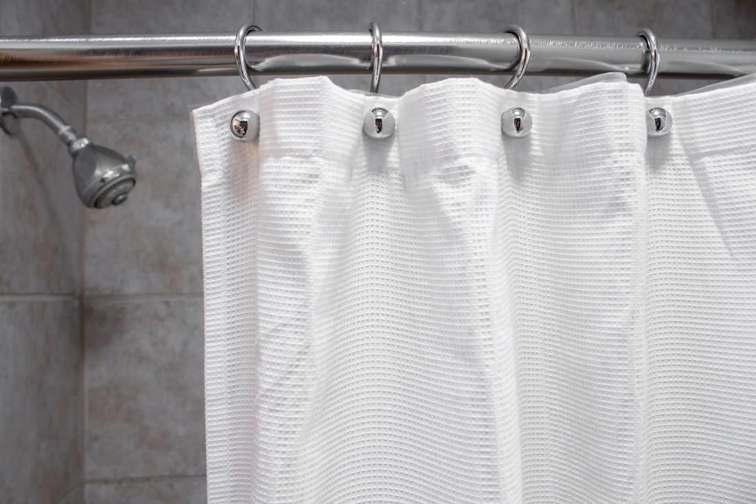 a white shower curtain in an empty shower with water OFF medium shot 