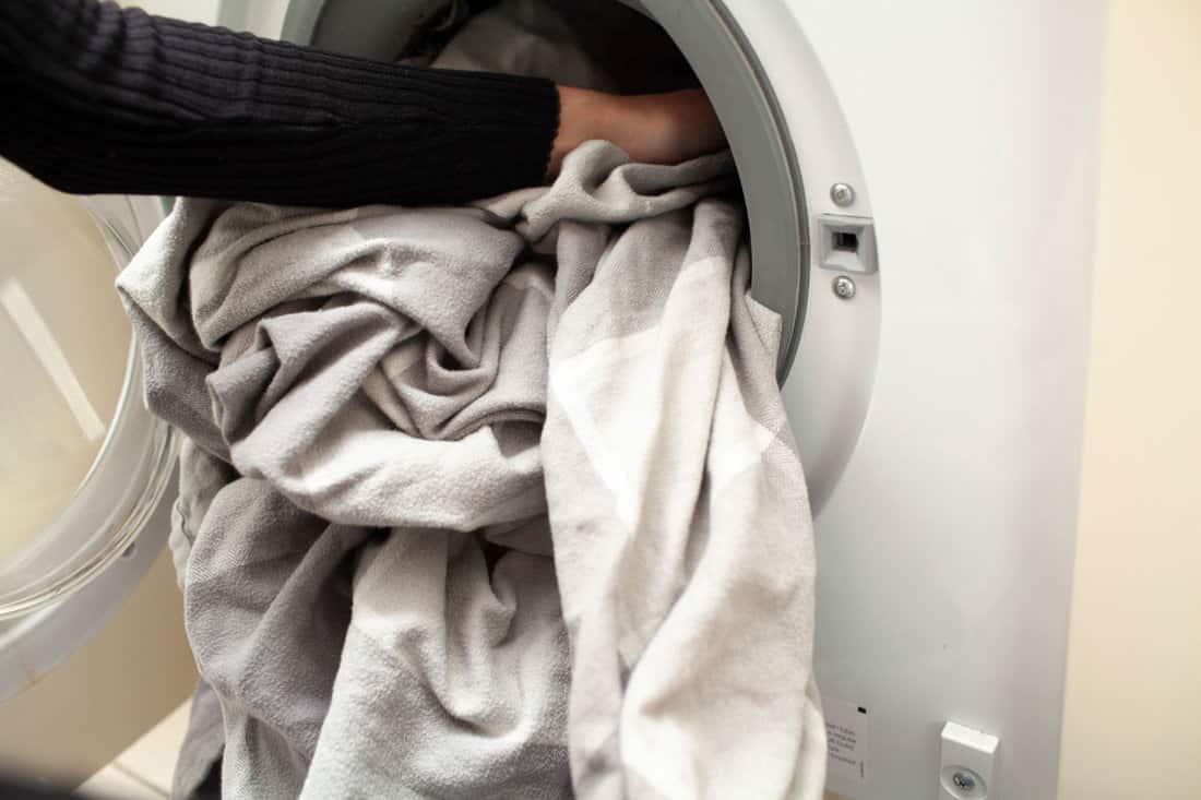 bed sheets being loaded into washing machine