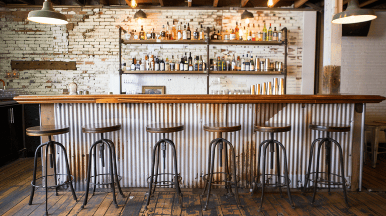 Four bar stools in front of a mini bar with tin roof as cladding. Basement has wooden flooring and white painted walls with exposed ceilings, 30 Awesome Rustic Basement Ideas [Photo List Inspiration] - 1600x900