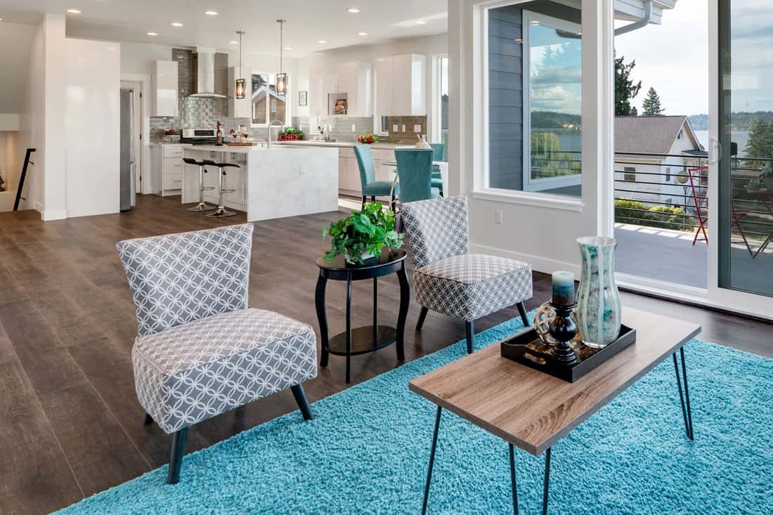 A gorgeous modern living room with wooden laminated flooring, blue colored carpet, and two patterned accent chairs