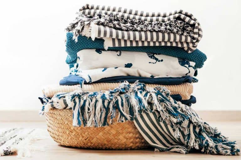 Blankets piled together in a basket, 15 Types of Blankets Every Homeowner Should Know