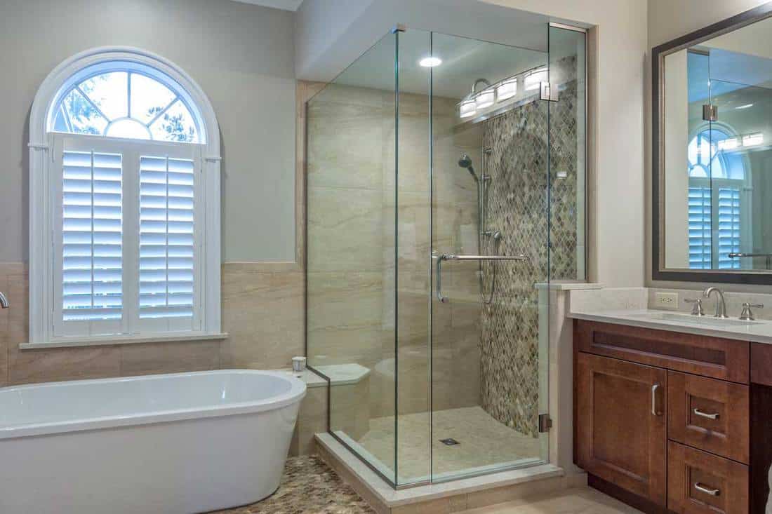 Modern bathroom with glass shower, bathtub and mirror above brown cabinet with white countertop washbasin, 13 Shower Curtain Alternatives You Need To Know About