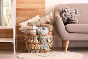 Basket with blankets and pillows near sofa indoors, How to Store Blankets [5 Easy Methods!]