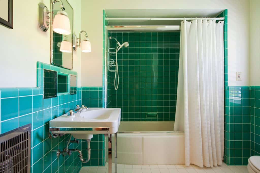 Interior of a jade and green themed bathoom with green bathroom tiles and a matching white curtain