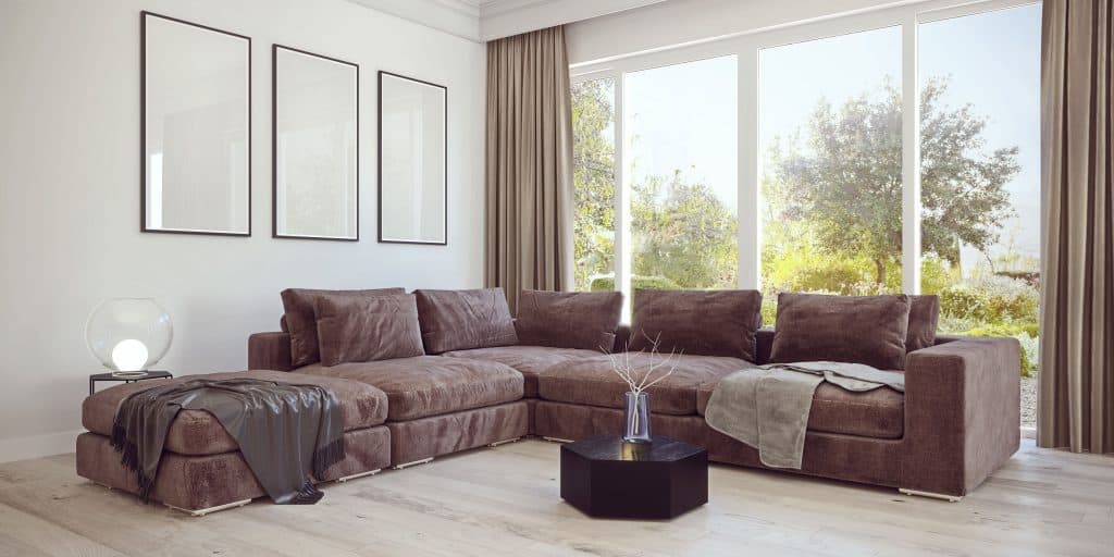 A brown sectional sofa inside a white walled living room with beige curtains
