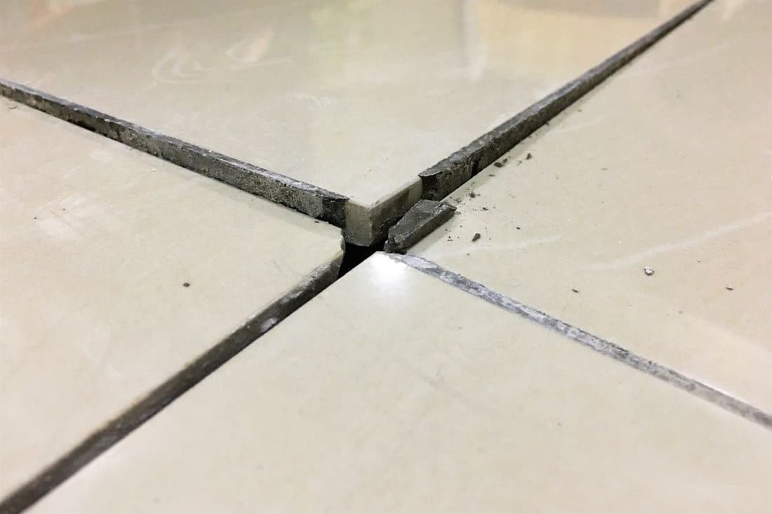 Close up of a cracked ceramic tiles on a residential house floor surface due to improper construction material.