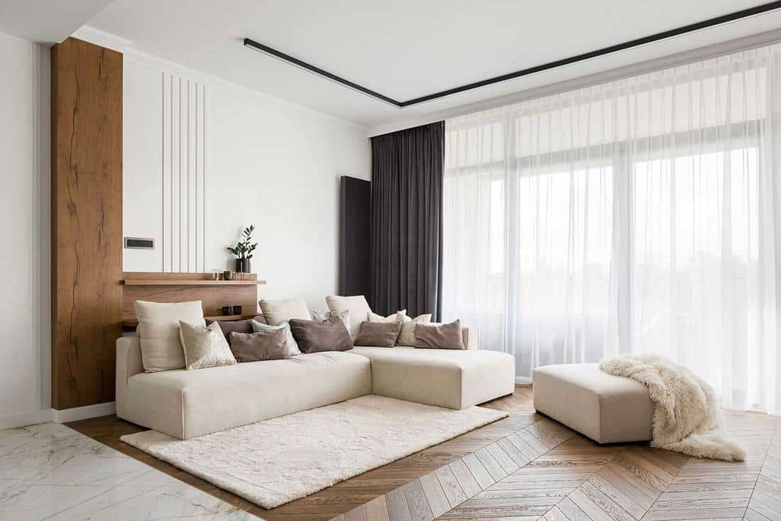 Salon élégant et confortable avec grand canapé d'angle, parquet et grandes fenêtres
