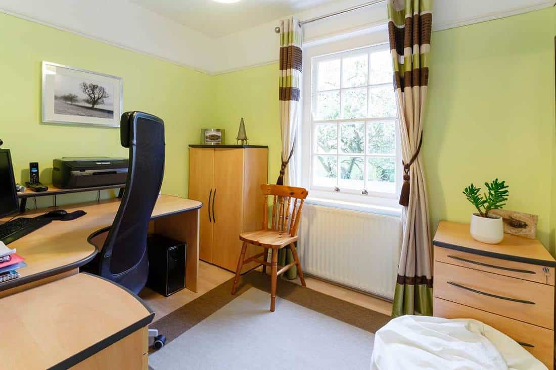 Home office with wooden interior, desktop, swivel high back office chair, green walls and window