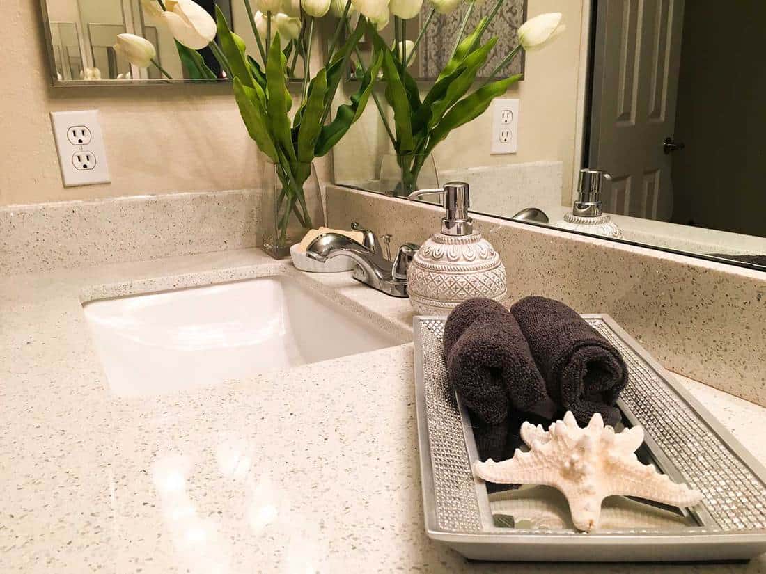 Modern bathroom sink with white tulips on vase, starfish and towels