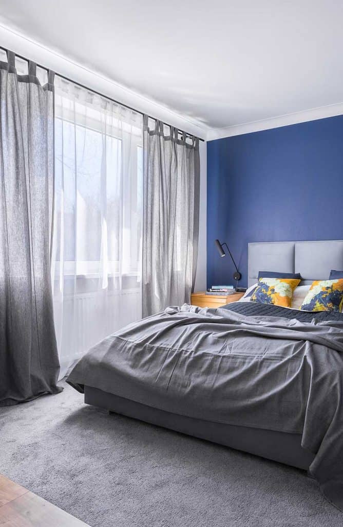 Modern cobalt blue bedroom with double bed, gray bedding, carpet and window