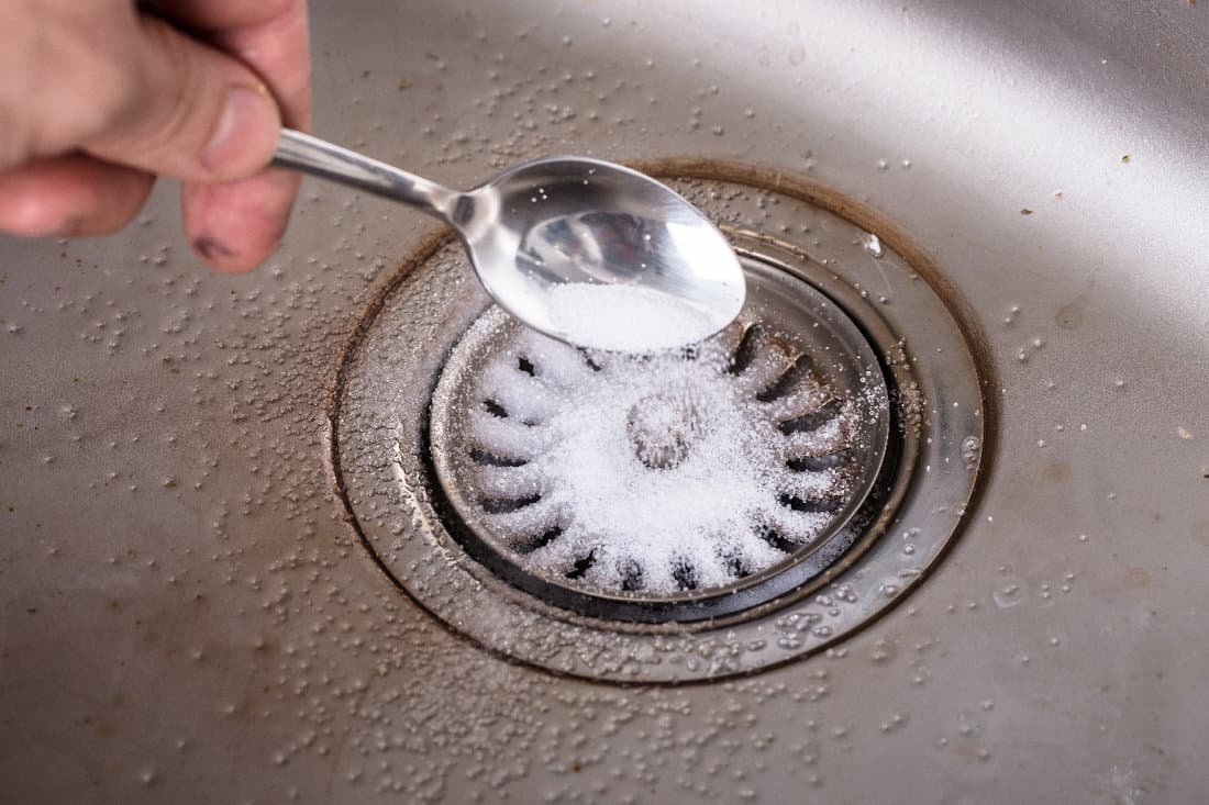 Person putting baking soda on drain In the sink