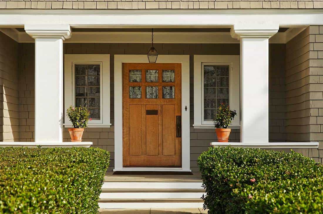 Concrete walkway bordered with hedged shrubs leads to wooden front door of a home