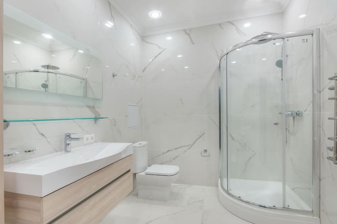 Contemporary master bathroom features a vanity cabinet fitted with rectangular sink and modern faucet under large mirror. Glass shower with rain shower head 