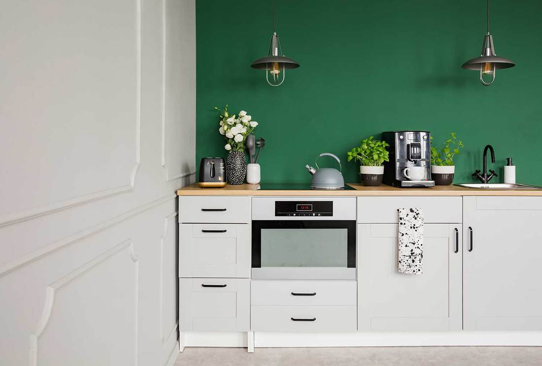 Elegante keuken met gasfornuis op witte kast, kamerplanten, industriële designlamp en koffiezetapparaat