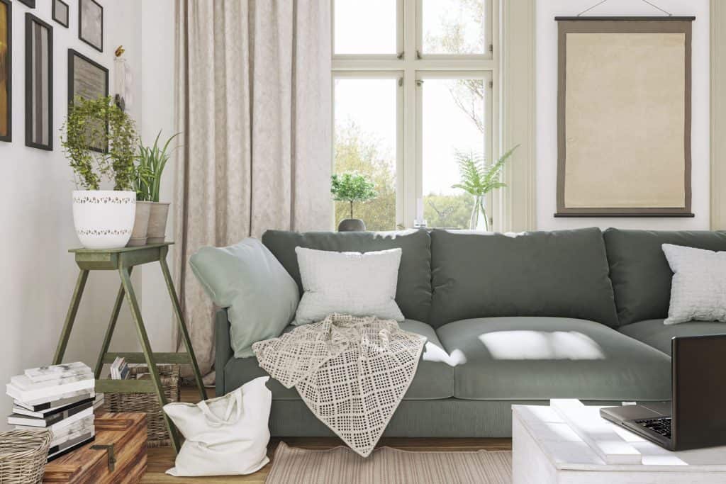 Interior of a modern living room with a green sofa, indoor plant, white and green throw pillows with a beige drape