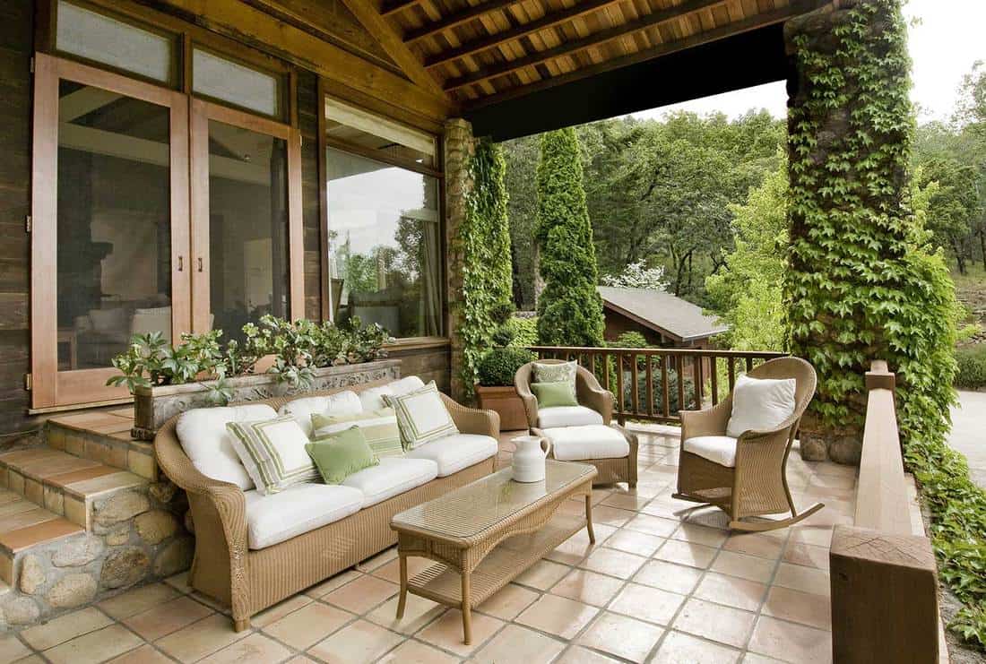 Maison moderne avec un joli porche, des doubles portes en bois, des meubles en osier et un sol en pavé de tuiles mexicaines