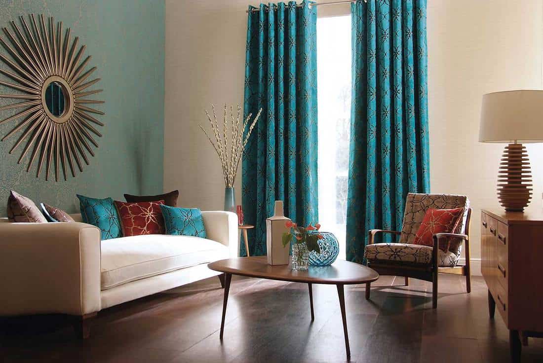 Contemporary living room with beige sofa, patterned teal curtains, round wooden table and vases