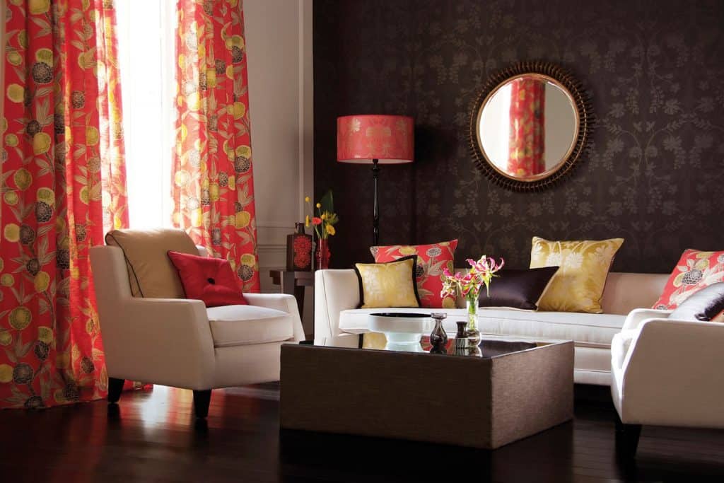 Dark living room with red floral curtains and white couches with circular mirror mounted at walls