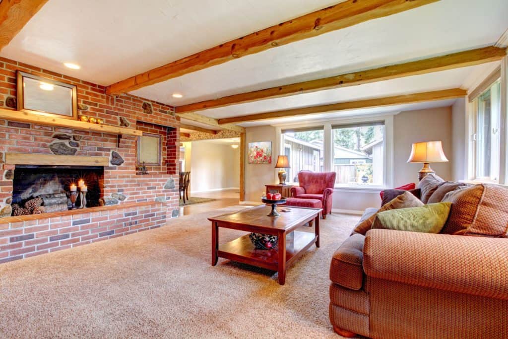 Large living room with fireplace decorated with brick wall and white ceiling with wooden trusses