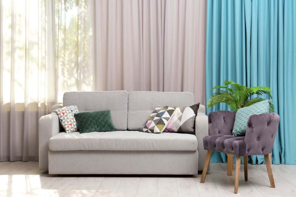 Light gray sectional sofa with patterned throw pillows and white curtains