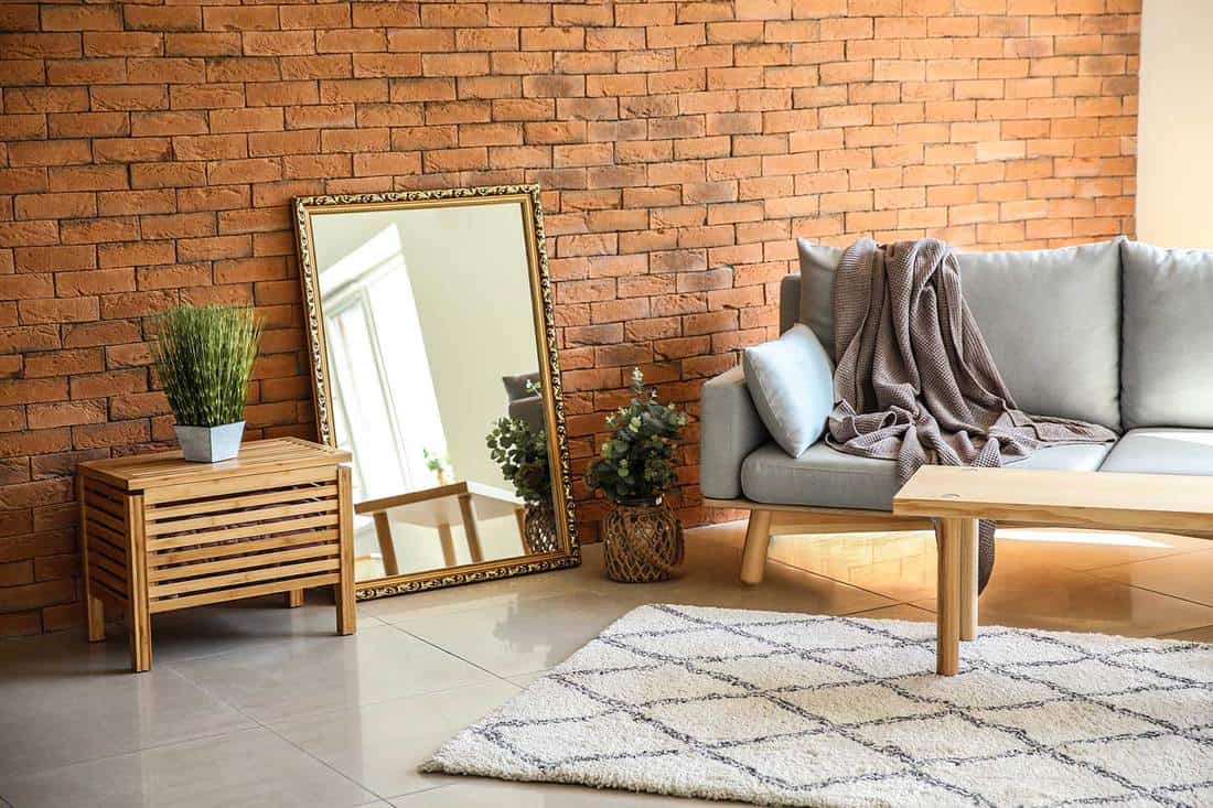 Living room interior with brick wall, big mirror and stylish furniture