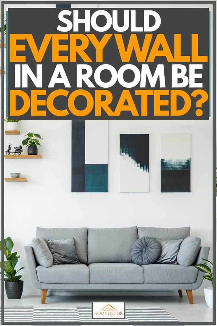 White wall with plants placed on dividers and cabinet and grey couch with blue paintings placed on wall, Should Every Wall In A Room Be Decorated?