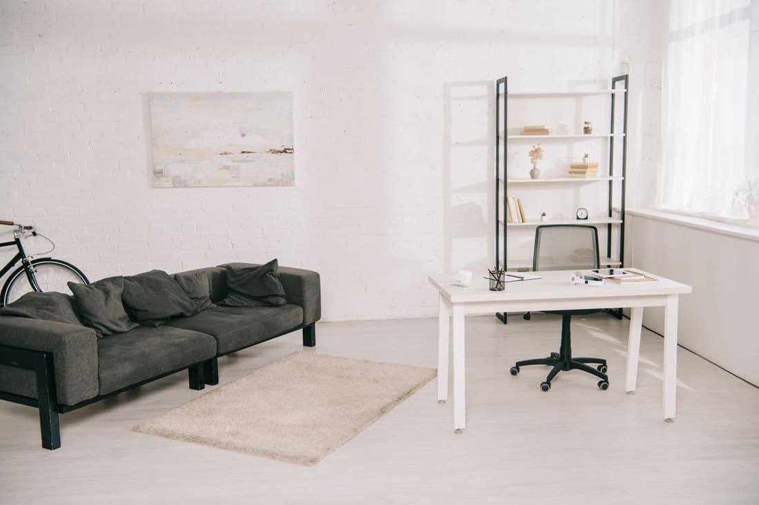 Salon spacieux avec canapé gris, table blanche et étagère avec livres 